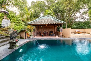 A pool area with a tiled roof structure, seating, and a statue. - Tanah Merah Art Resort (Ubud)