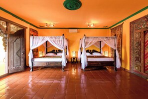 A room with two beds, each with a canopy, and a wooden door with intricate carvings. - Tanah Merah Art Resort (Ubud)