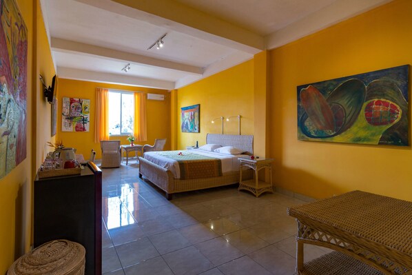 A hotel room with a bed, a desk, a chair, and a painting on the wall. - Tanah Merah Art Resort (Ubud)