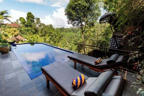 A pool area with lounge chairs and a view of a lush forest. - Tanah Merah Art Resort (Ubud)
