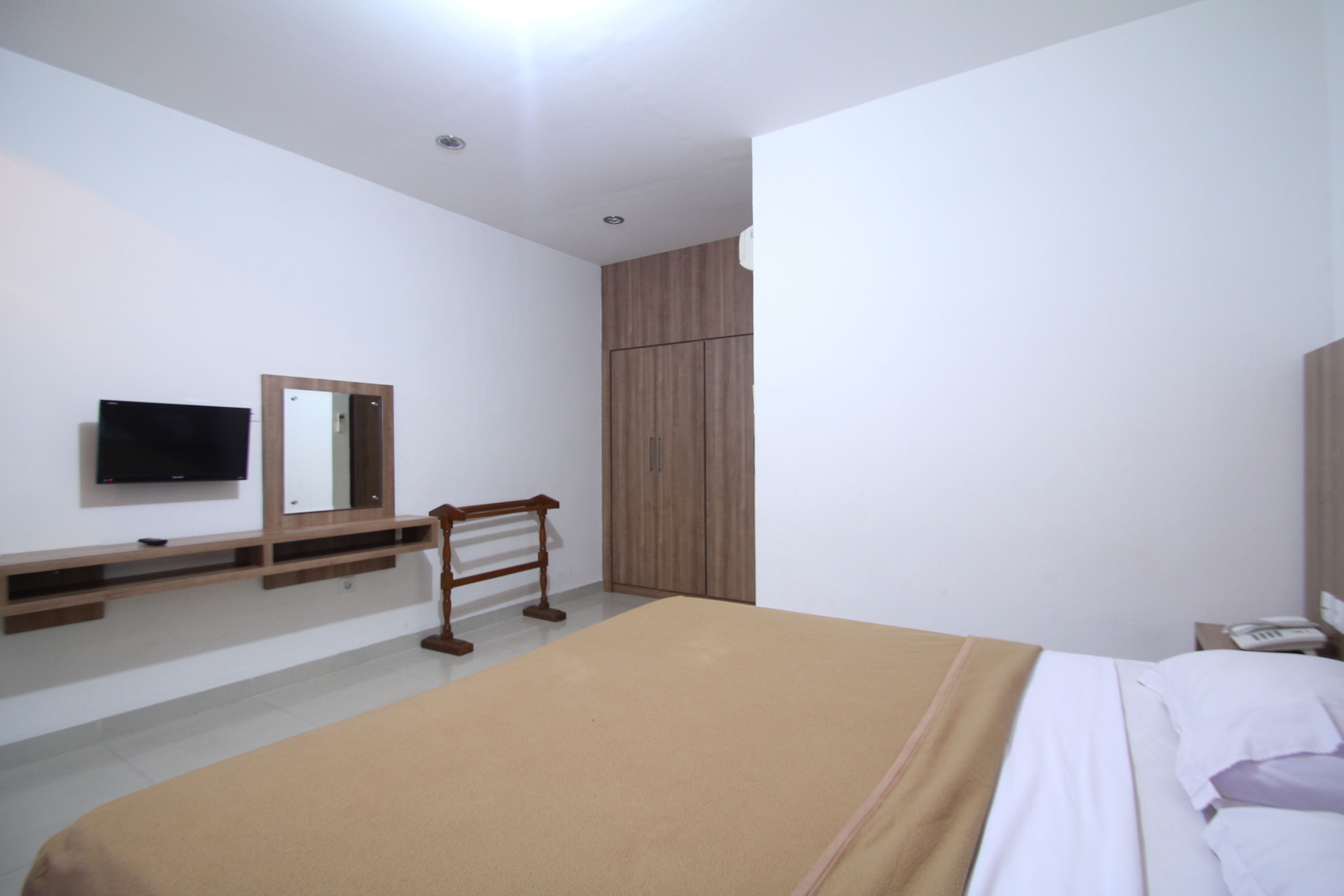 A bedroom with a bed, a TV mounted on the wall, a wardrobe, and a bedside table.