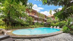 Una piscina rodeada de abundante vegetación, con un edificio de varios pisos al fondo.