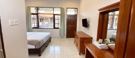 A hotel room with a bed, a wooden desk, a television mounted on the wall, and a window with curtains.