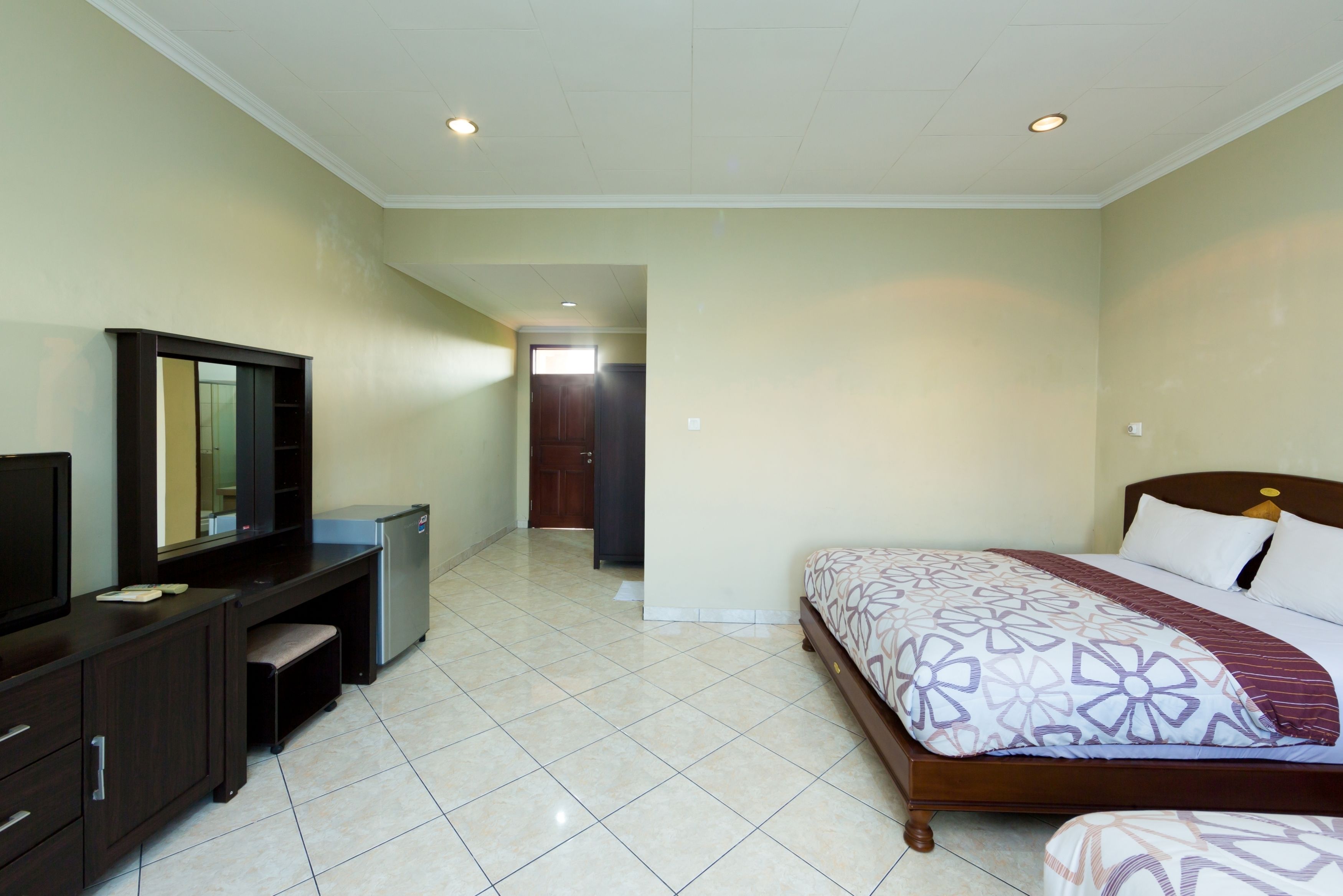 A bedroom with a bed, a desk, a mirror, and a door leading to another room.
