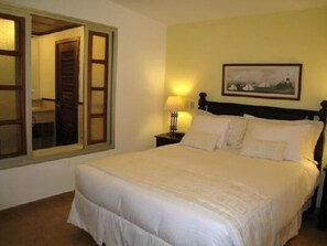 Cama bem arrumada com lençóis brancos, abajur e um quadro na parede.