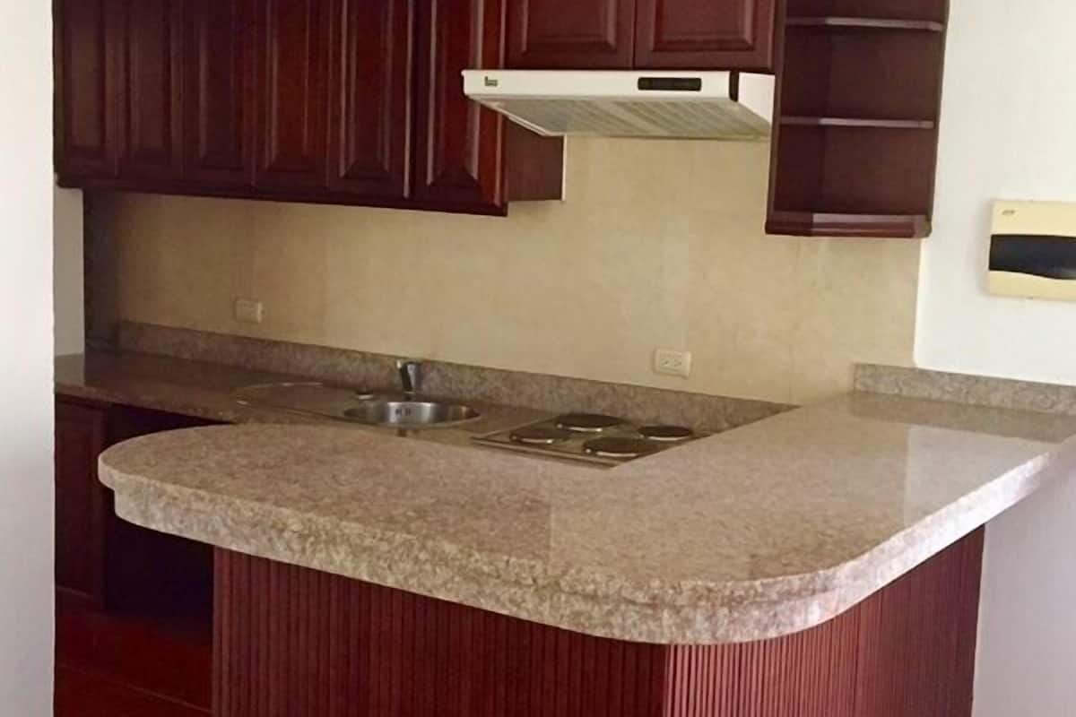 A kitchen with dark wooden cabinets, a granite countertop, a stainless steel sink, and a range hood.