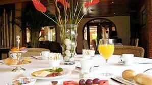 Uma mesa de café da manhã posta para dois, com pratos de fruta, pão e um copo de suco de laranja.