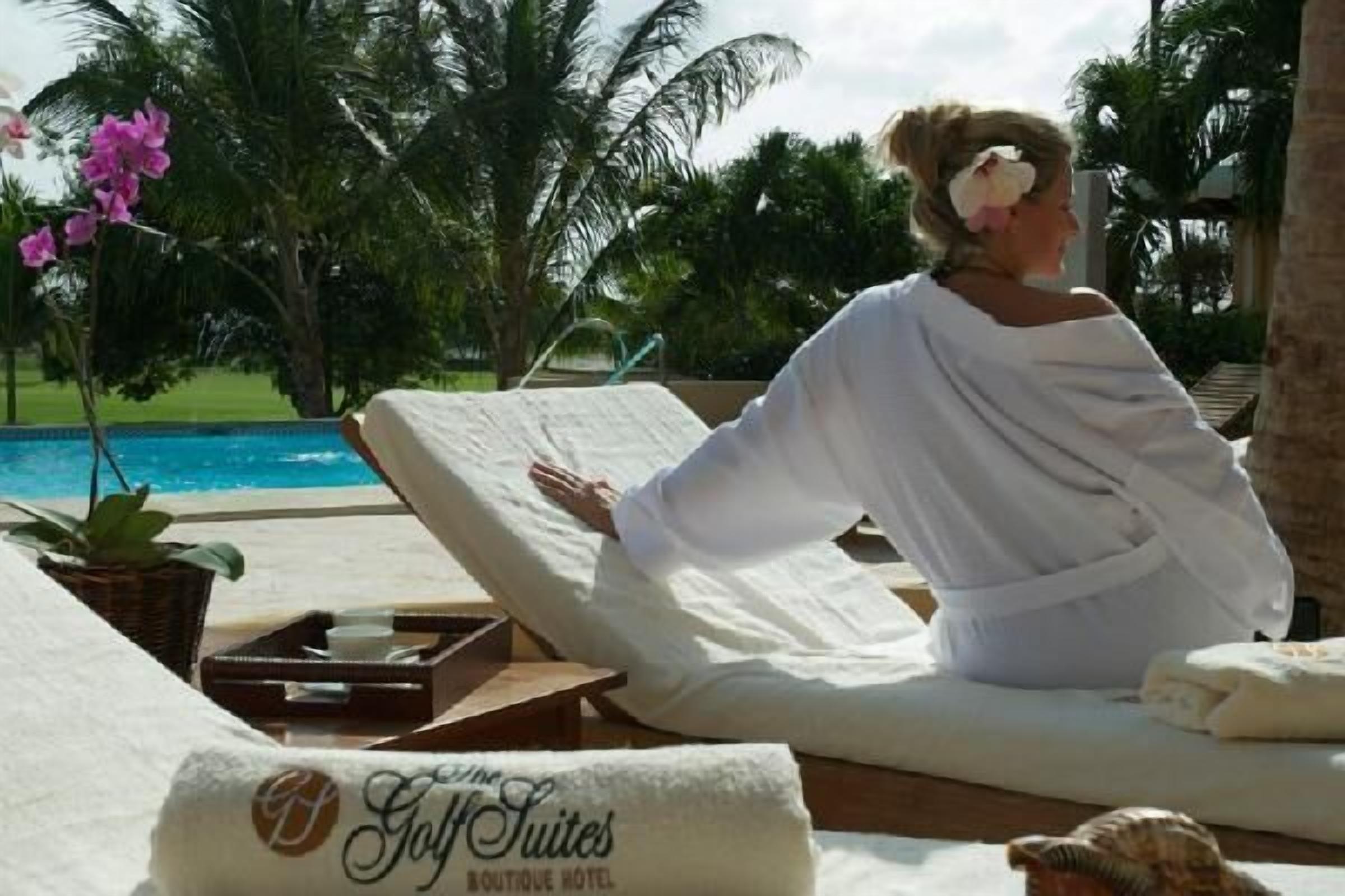 A person relaxing on a sun lounger by a pool with a tropical garden view.