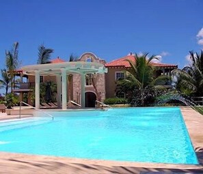 Ein Schwimmbecken mit einer Pergola, Palmen und einem Gebäude mit rotem Dach.