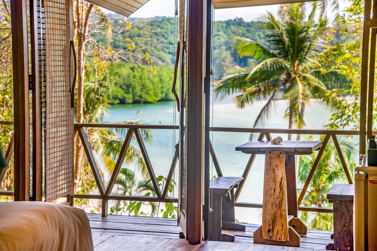 A wooden deck with a table and benches, overlooking a lake and palm trees.