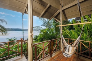 A wooden deck with a hammock chair, overlooking a beach and lush greenery.