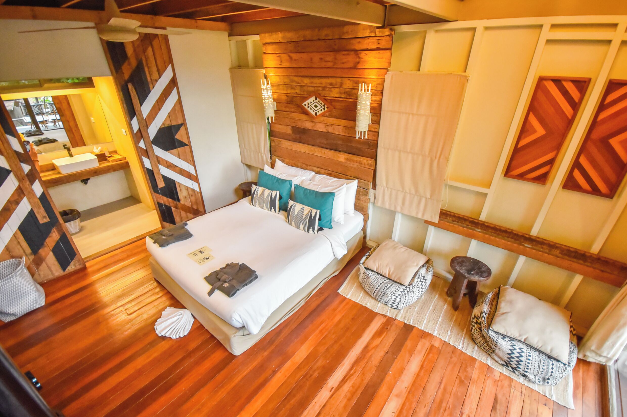 A bedroom with a wooden floor, a bed with pillows, a nightstand, a small table, and a wall with geometric patterns.