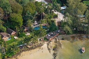 An aerial view of a resort with a swimming pool, palm trees, and a beach.