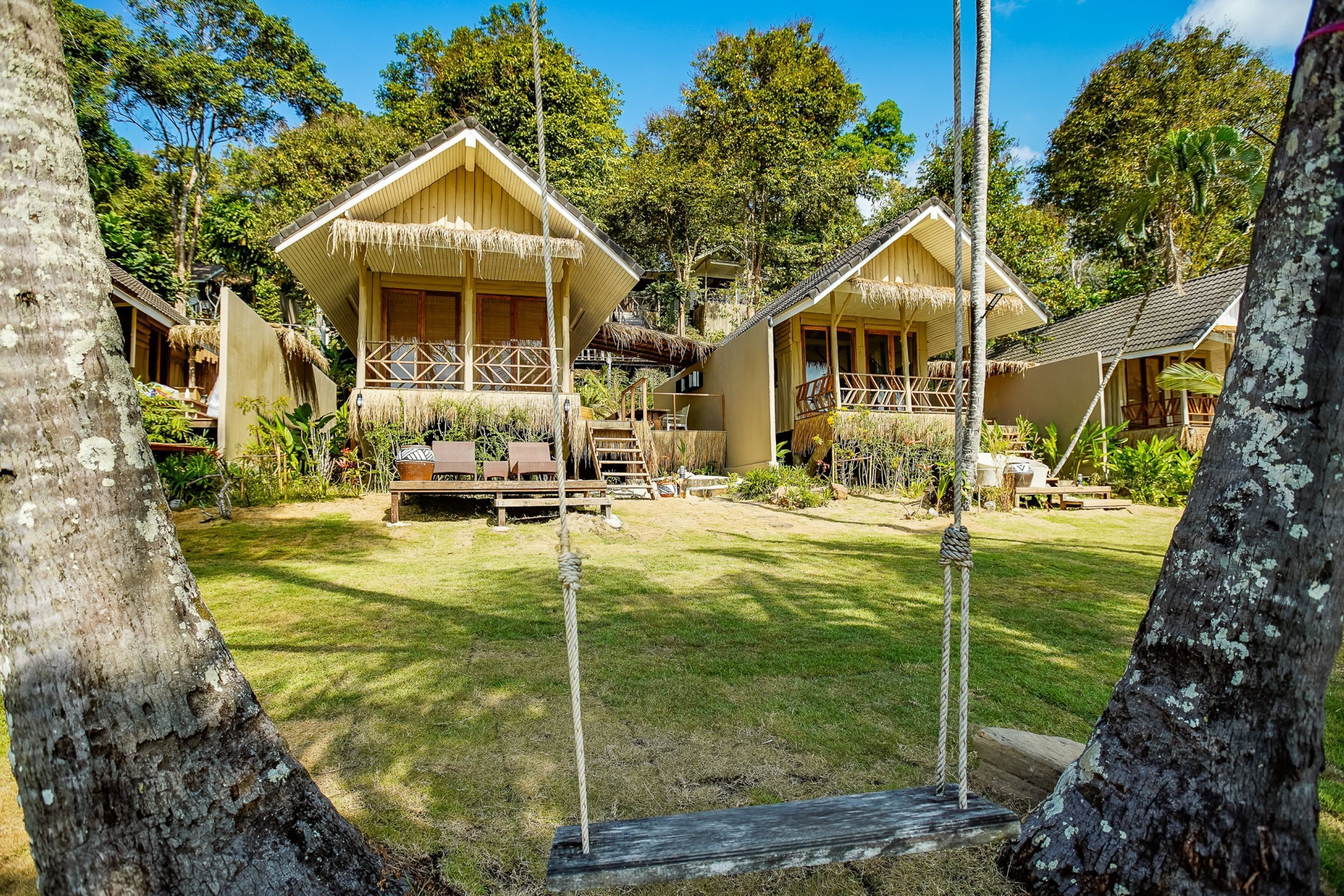 Een resort met houten bungalows, een gazon en een touwschommel.