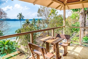 A wooden table and bench on a balcony with a view of a beach and palm trees.