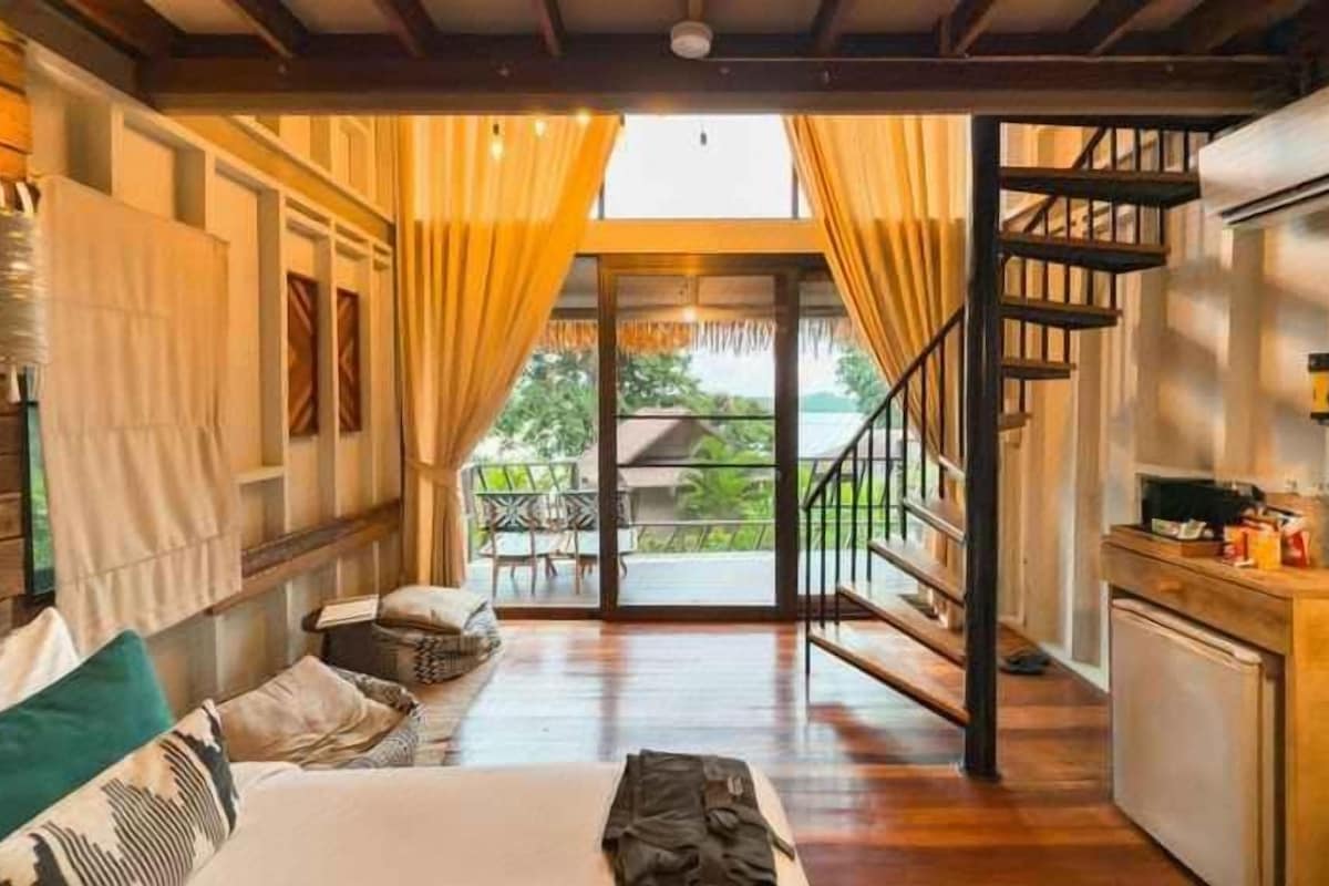 A spacious living area with a sofa, a dining table, and a staircase leading to a balcony.