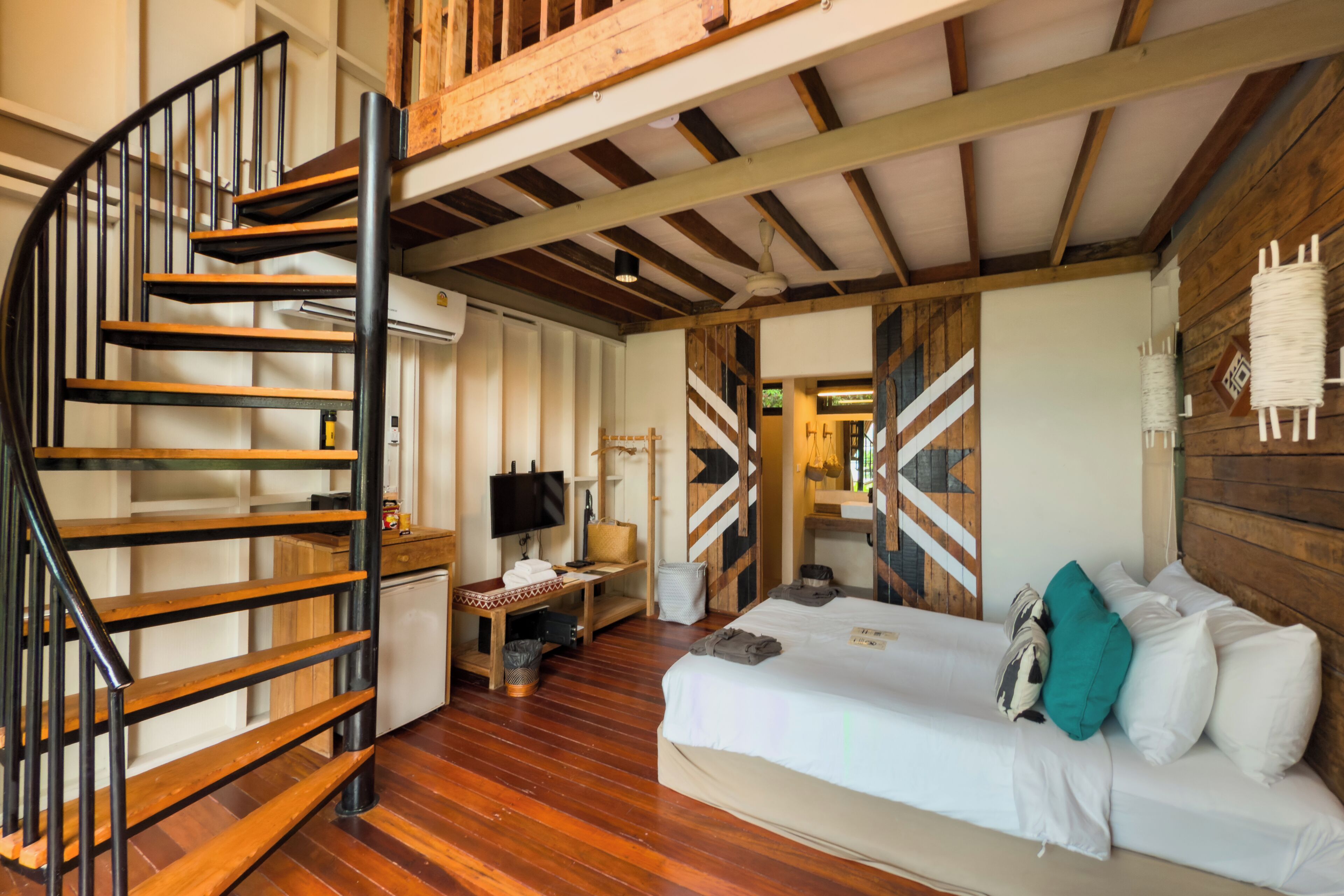 A bedroom with a wooden staircase, a bed with pillows, a desk with a computer, and a TV.