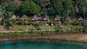 A resort with multiple bungalow-style accommodations, a clear view of the surrounding lush greenery, and a body of water in the foreground.