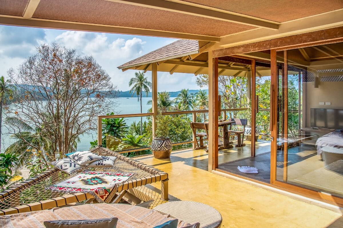 Un balcon spacieux offrant une vue sur la mer, aménagé avec une table et des chaises, et une porte vitrée donnant accès à une chambre.