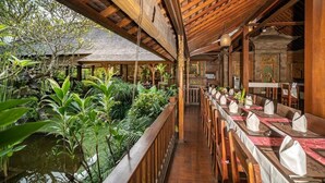 Un restaurant avec une longue table en bois, dressée pour le repas, entourée d’une végétation luxuriante et d’un petit étang.
