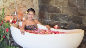 Une baignoire remplie de pétales de fleurs et entourée de bougies, le tout installé devant un mur de pierre.