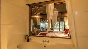 Une salle de bain avec une grande baignoire, un miroir qui reflète une chambre à coucher et une plante en pot.