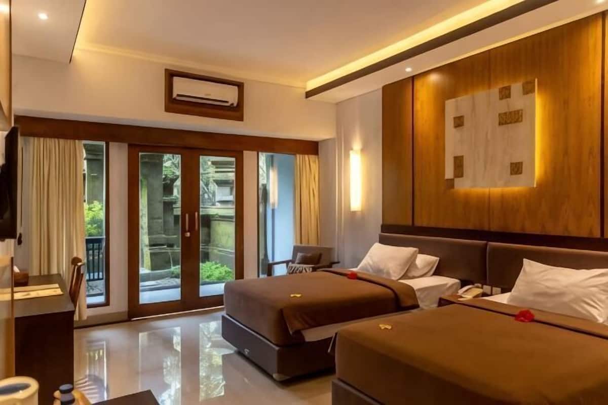 A hotel room with a bed, bedside table, and a view through a sliding door to an outdoor area.
