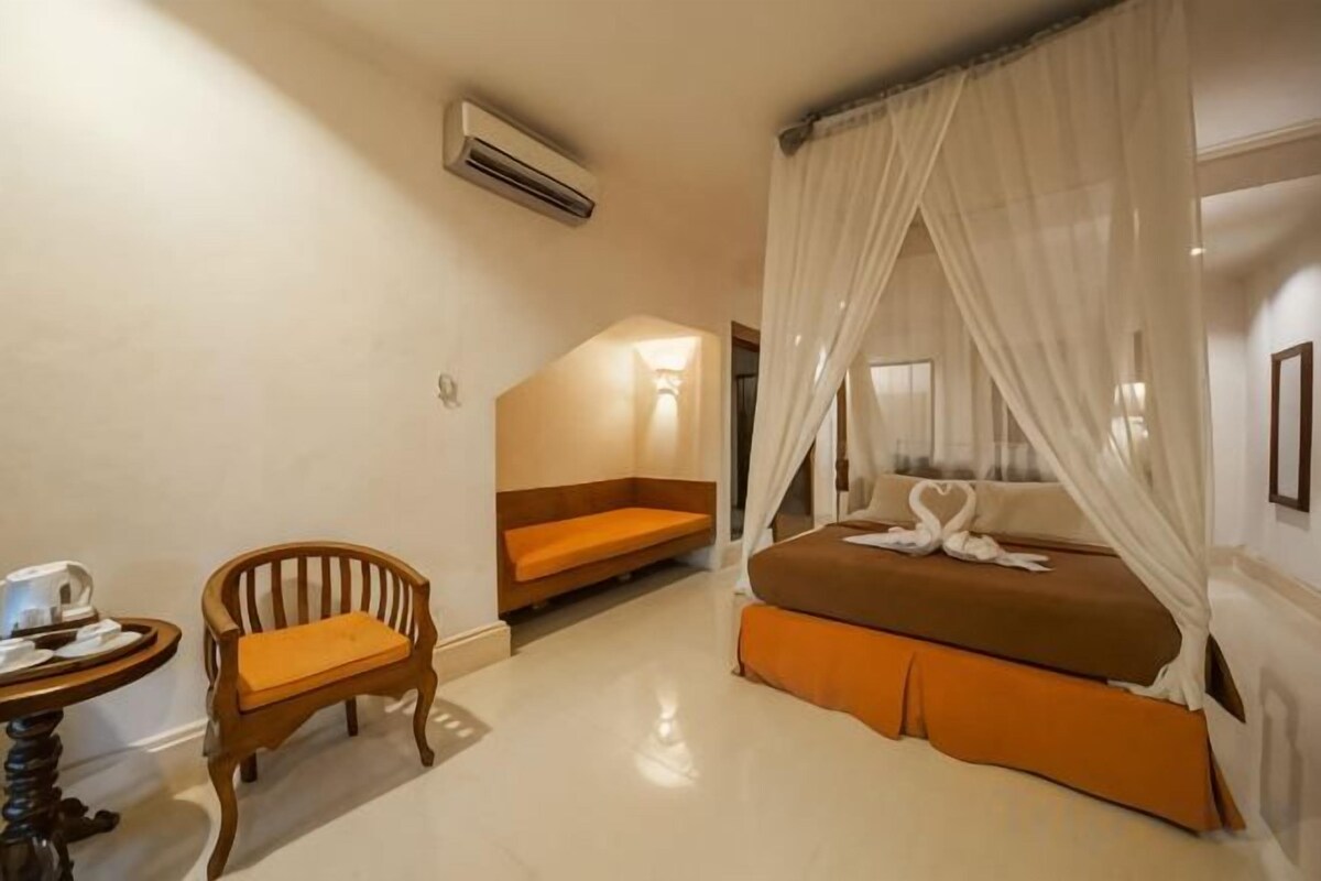 A hotel room with a bed, a chair, a small table, and a bench.