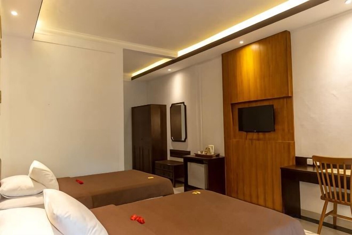 A hotel room with two single beds, a desk, a chair, a TV, and a wardrobe.