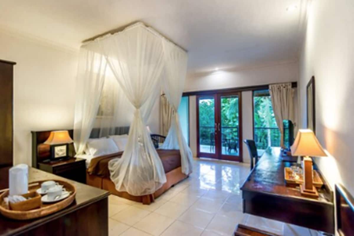 A bedroom with a canopy bed, a desk with a lamp, and a view of the outdoors.