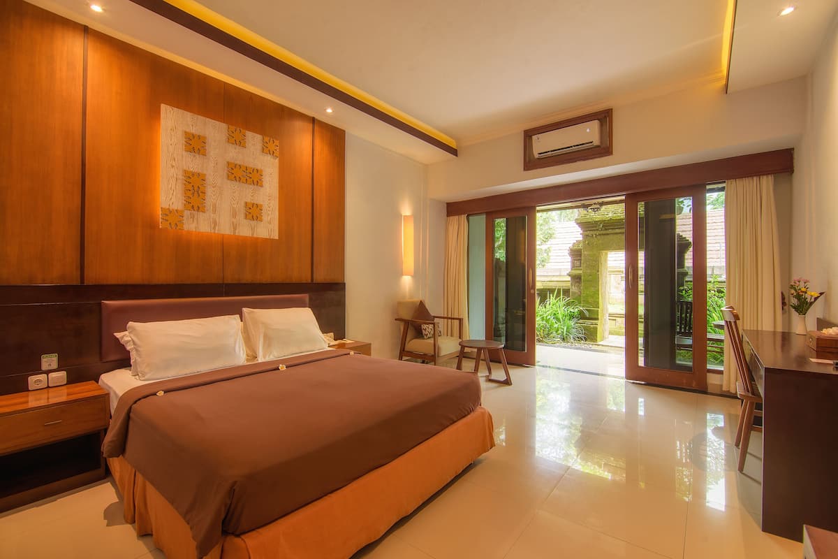 A hotel room with a large bed, a desk, and a view of the garden through the sliding doors.