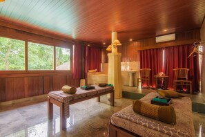 A room with a wooden ceiling, a bench, a bed with patterned bedding, a bathtub, and a window with curtains.