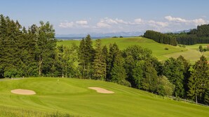 A golf course with sand bunkers, surrounded by dense forests and distant mountains under a clear sky. - CityHotel Kempten (Kempten)
