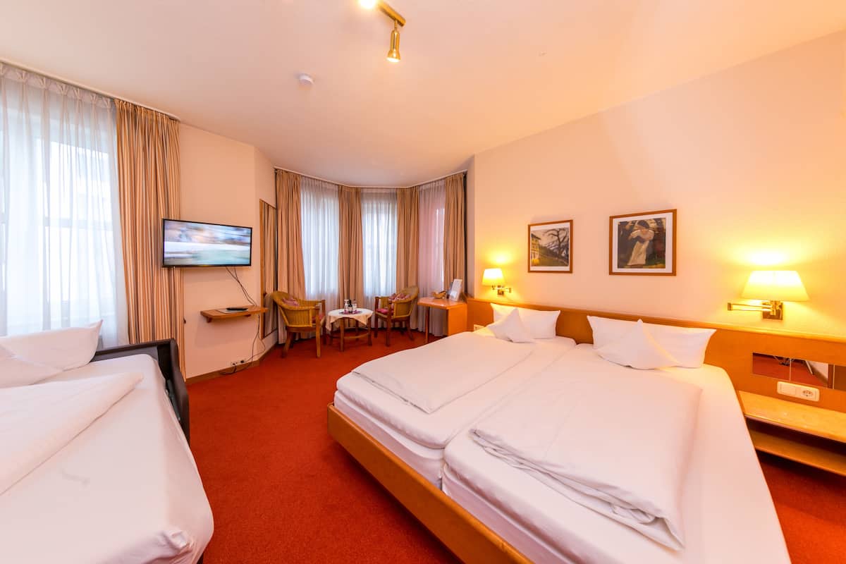 A hotel room with a large bed, a desk, a chair, a TV, and two paintings on the wall.