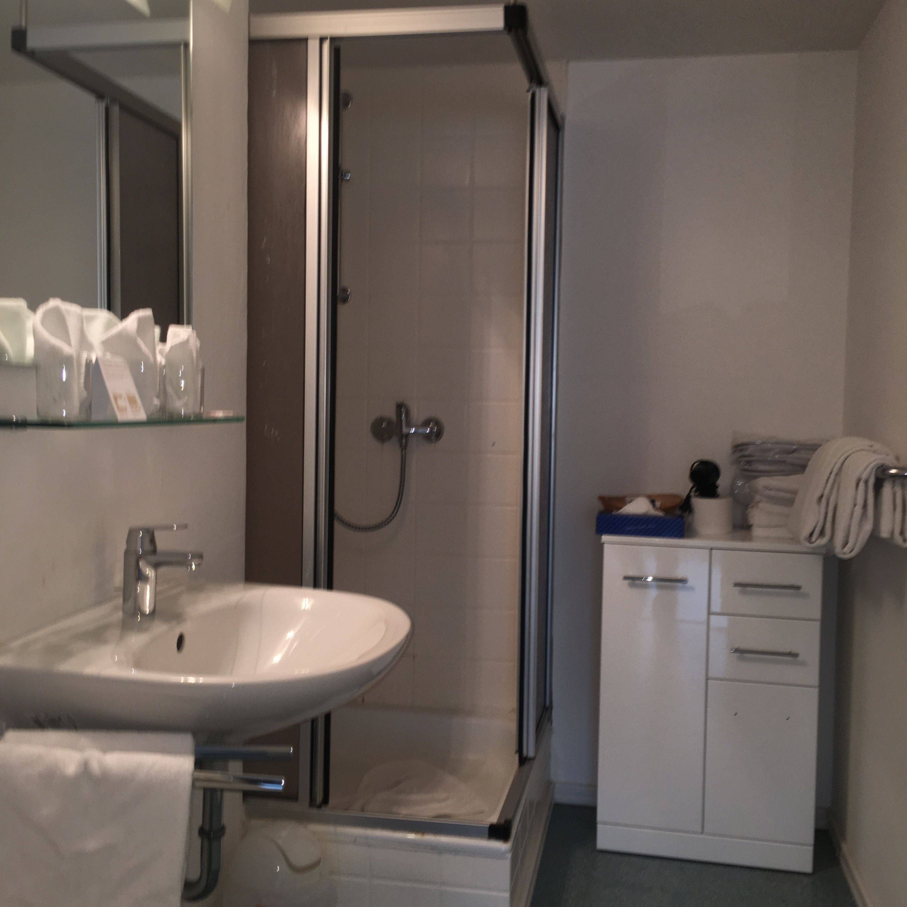 A bathroom with a sink, mirror, shower, and a cabinet with towels.