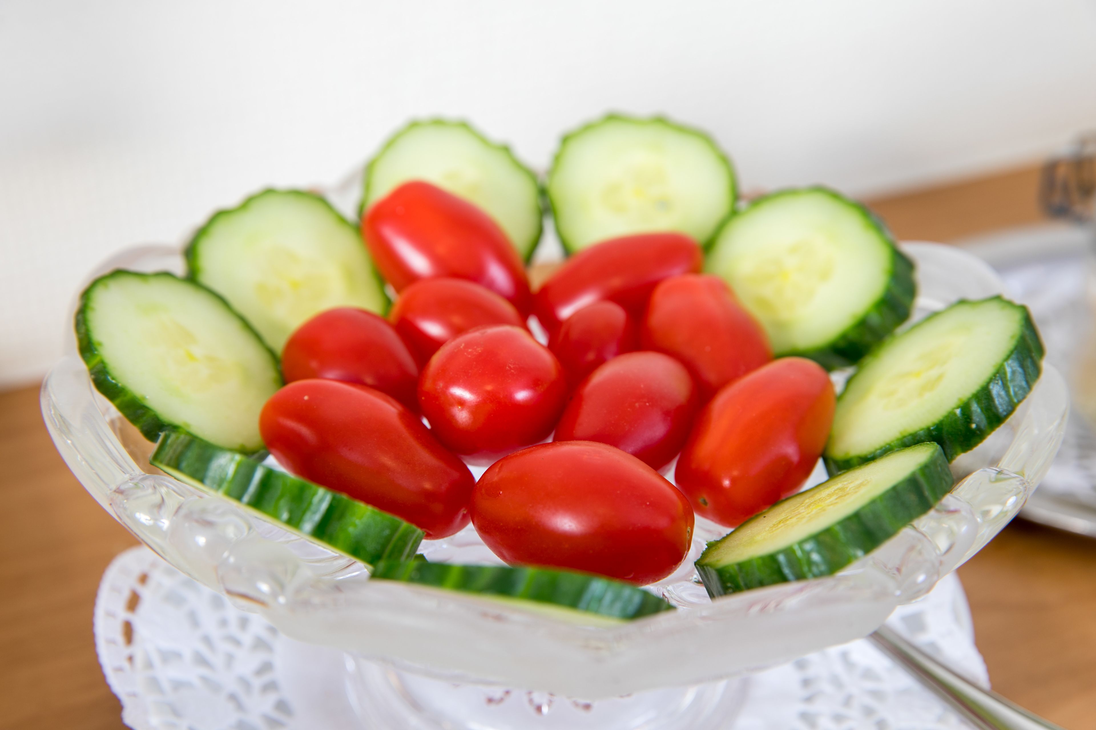 Une assiette en verre sur laquelle sont disposés des concombres en tranches et des tomates cerises, formant un motif décoratif.
