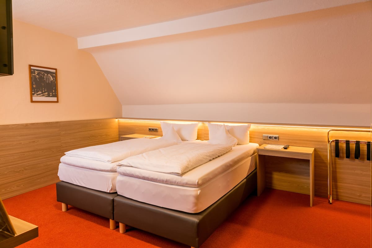 A modern hotel room with a double bed, a bedside table, a nightstand, and a wooden headboard.