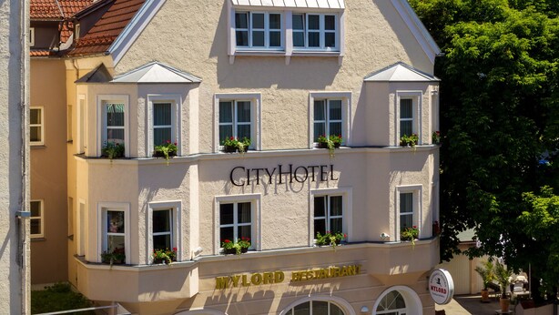 A two-story City Hotel with a classic European architectural style, featuring a prominent entrance with a sign, multiple windows, and balconies with potted plants. - CityHotel Kempten (Kempten)