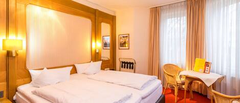Una habitación de hotel con una cama grande, un escritorio con una silla y un ventanal con cortinas.