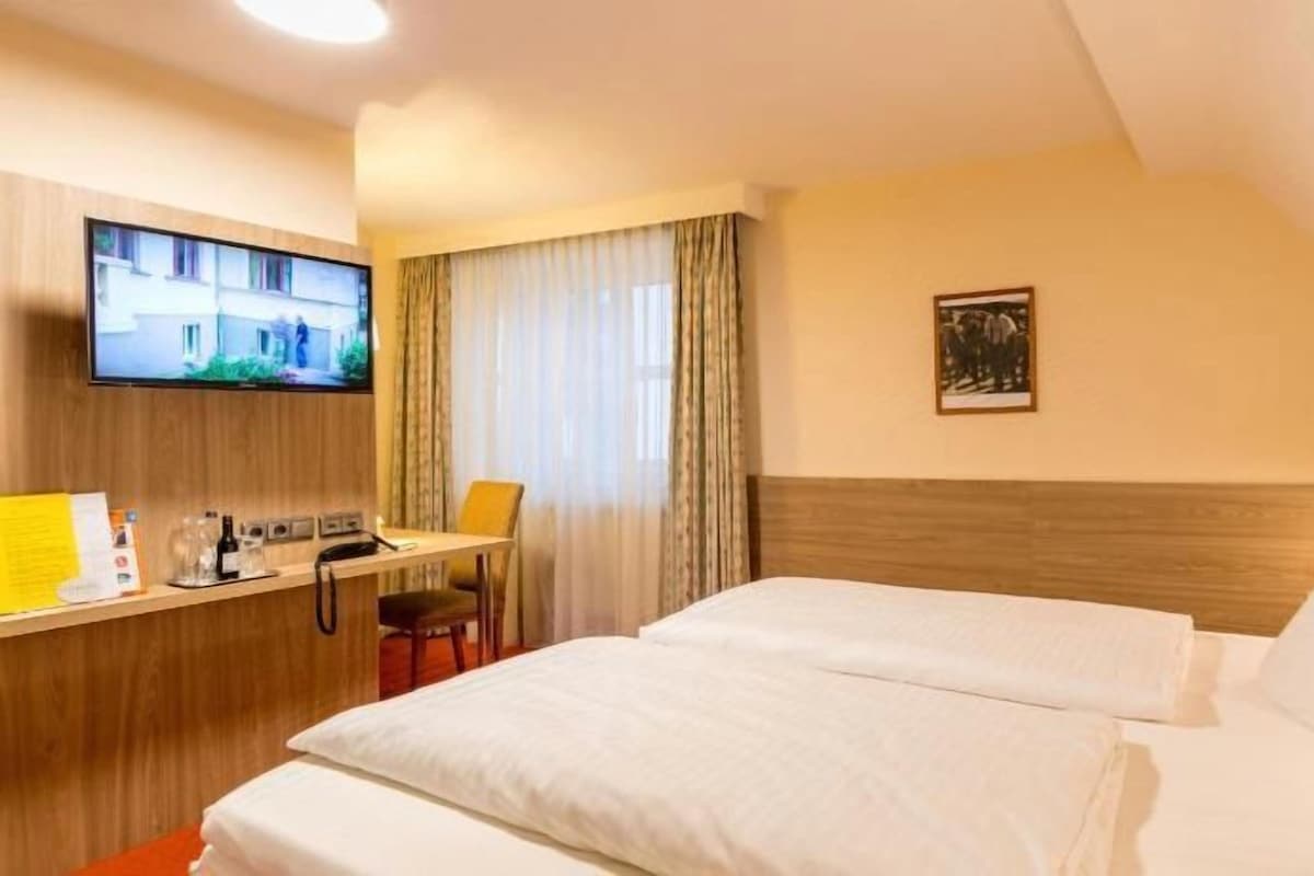 Une chambre d’hôtel avec deux lits, un bureau avec une chaise, une télévision et une fenêtre avec des rideaux.
