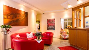 A lobby with red sofas, a large abstract painting, a poster, and a reception desk. - CityHotel Kempten (Kempten)