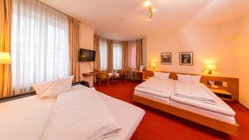 A hotel room with two beds, a desk, a chair, and a TV.