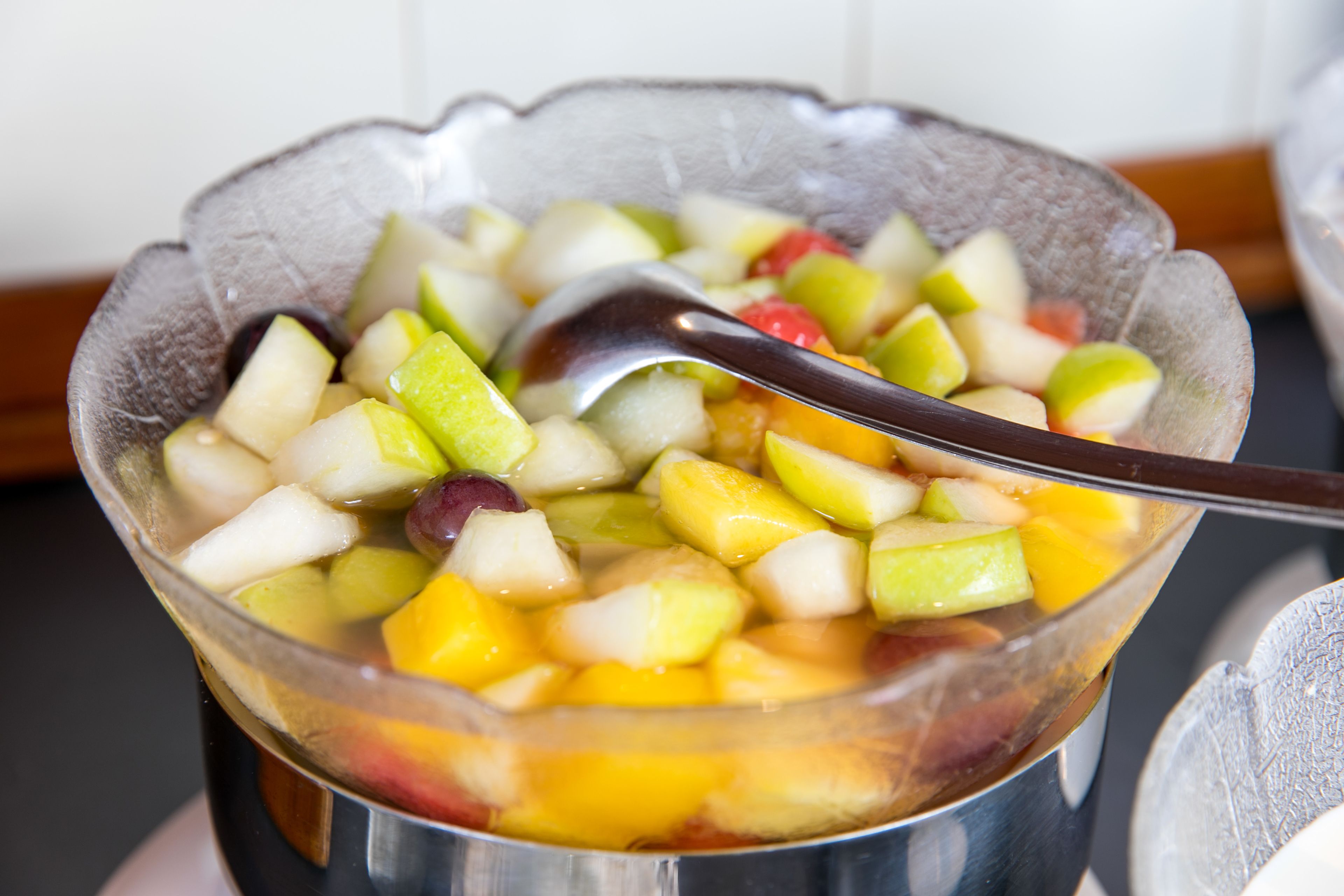 Un tazón de ensalada de frutas con una cuchara.