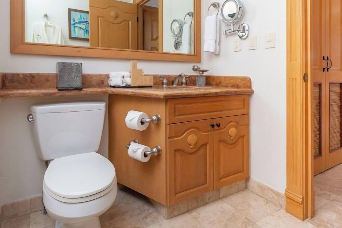 A bathroom with a toilet, wooden vanity, and a large mirror.