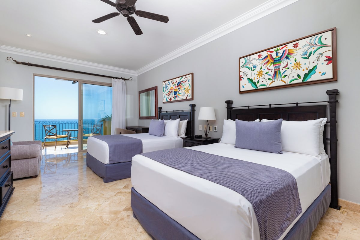A hotel room with two beds, a balcony, and artwork on the walls.