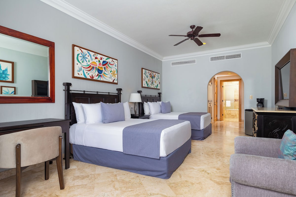 A hotel room with two beds, a desk, a chair, and artwork on the walls.