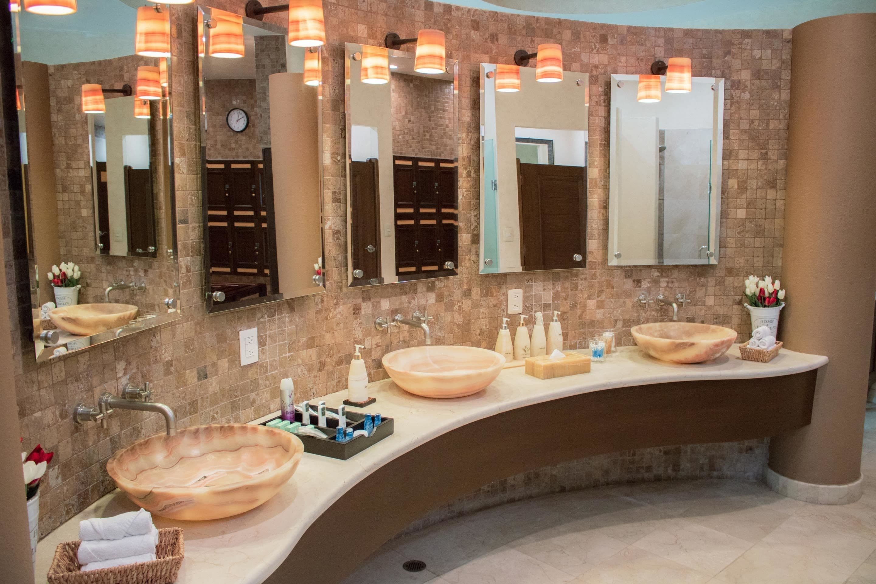 A modern bathroom with three large, oval-shaped sinks, multiple mirrors, and warm lighting.