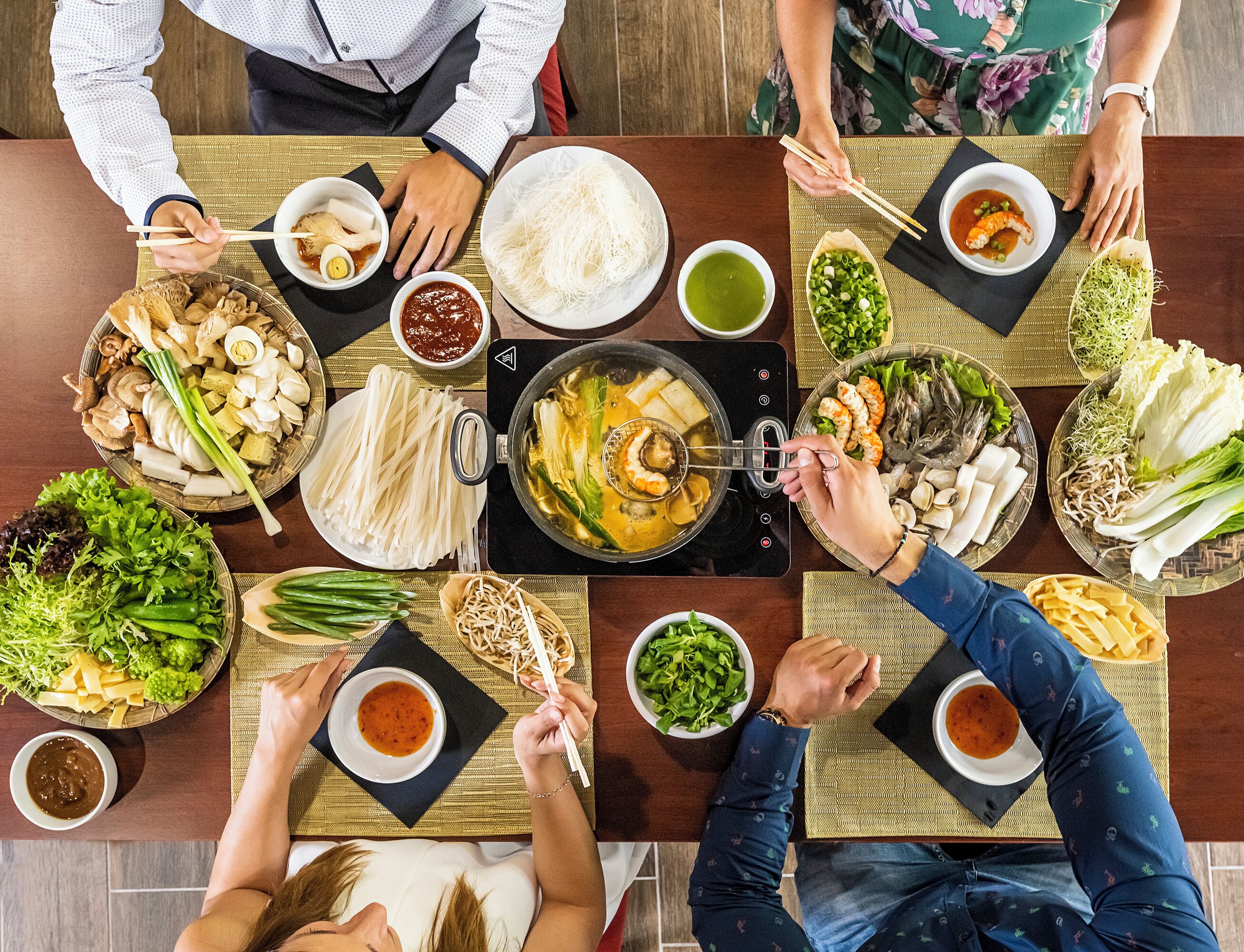 A group of people dining at a table with various dishes, including noodles, seafood, and vegetables.
