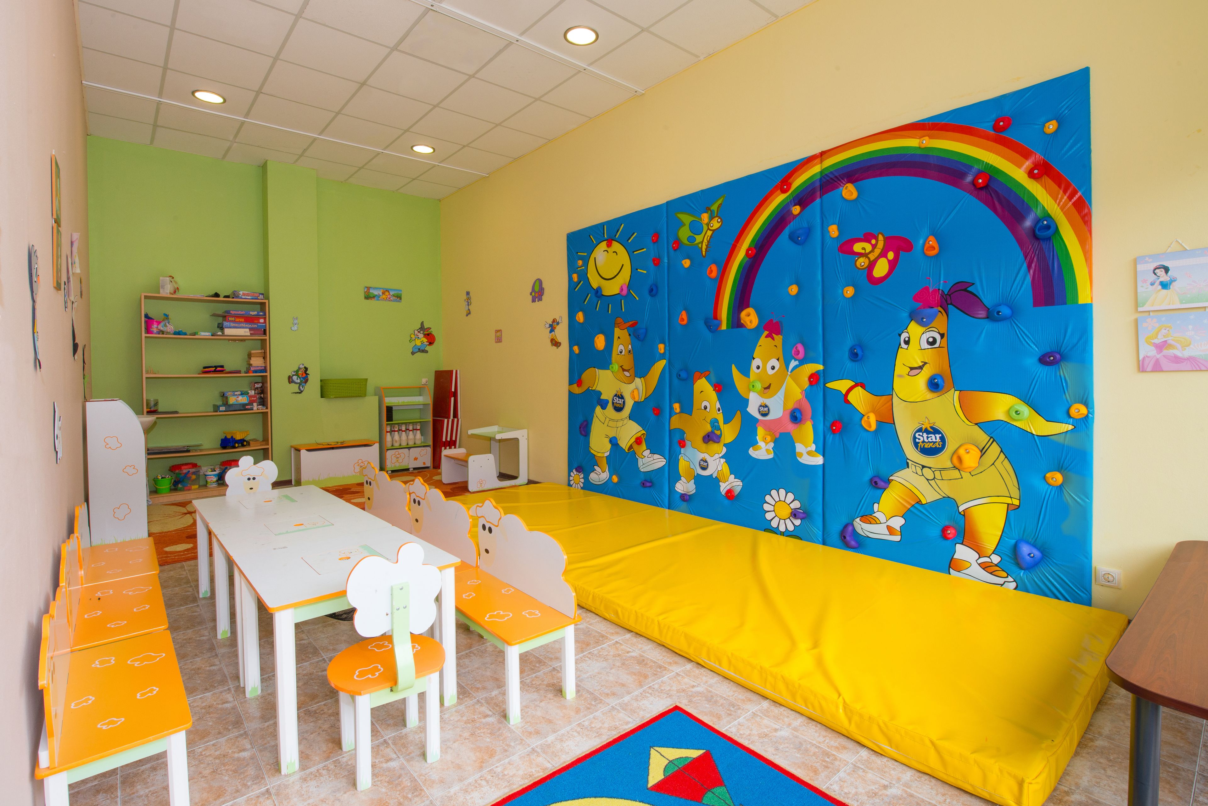 Un salón infantil con un gran mural, una zona de juegos y una mesa de comedor con sillas.