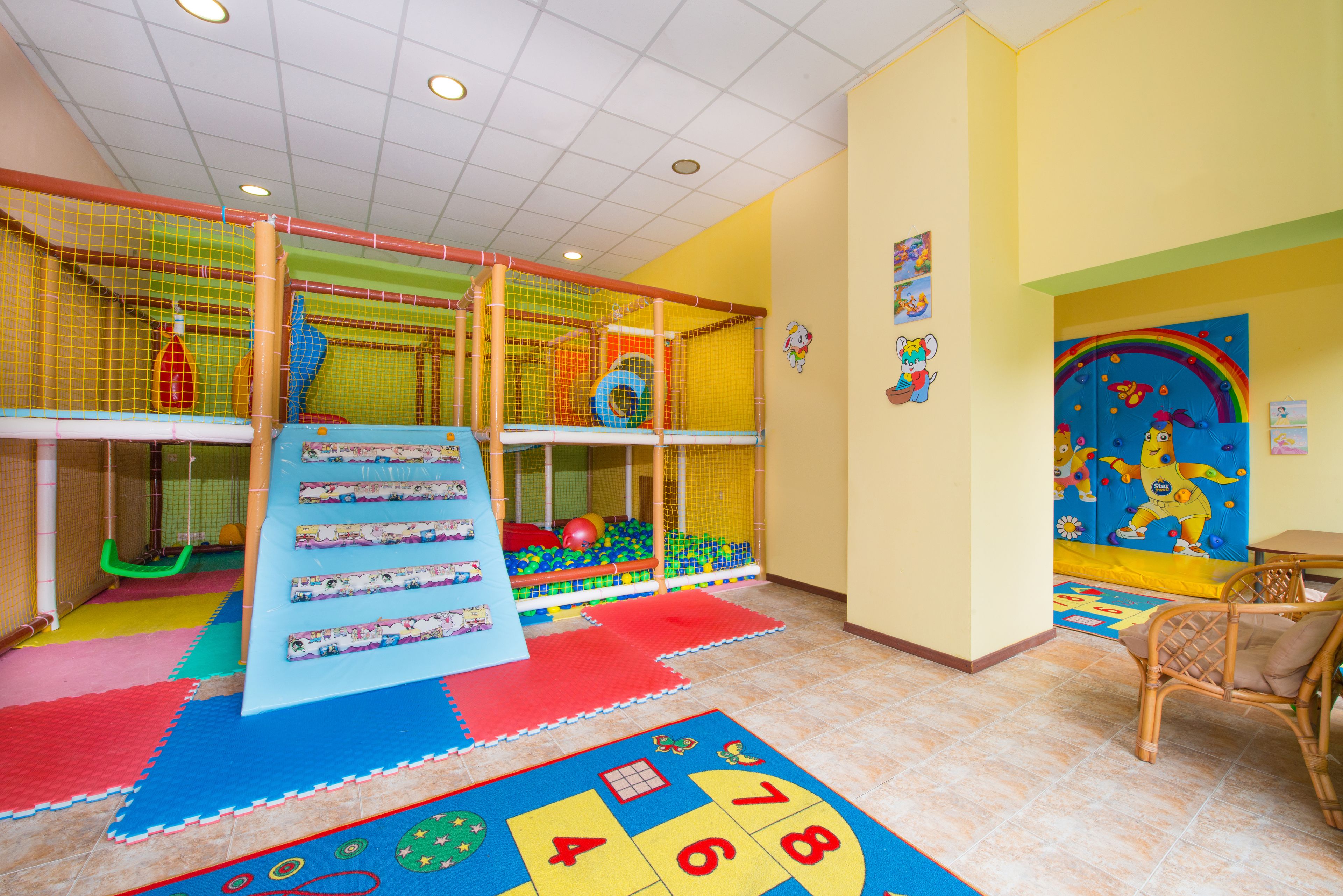 A children's play area with a slide, climbing net, and colorful mats.